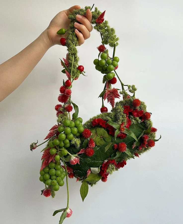 A botanical bag-like object formed from red flowers, green leaves and berries.