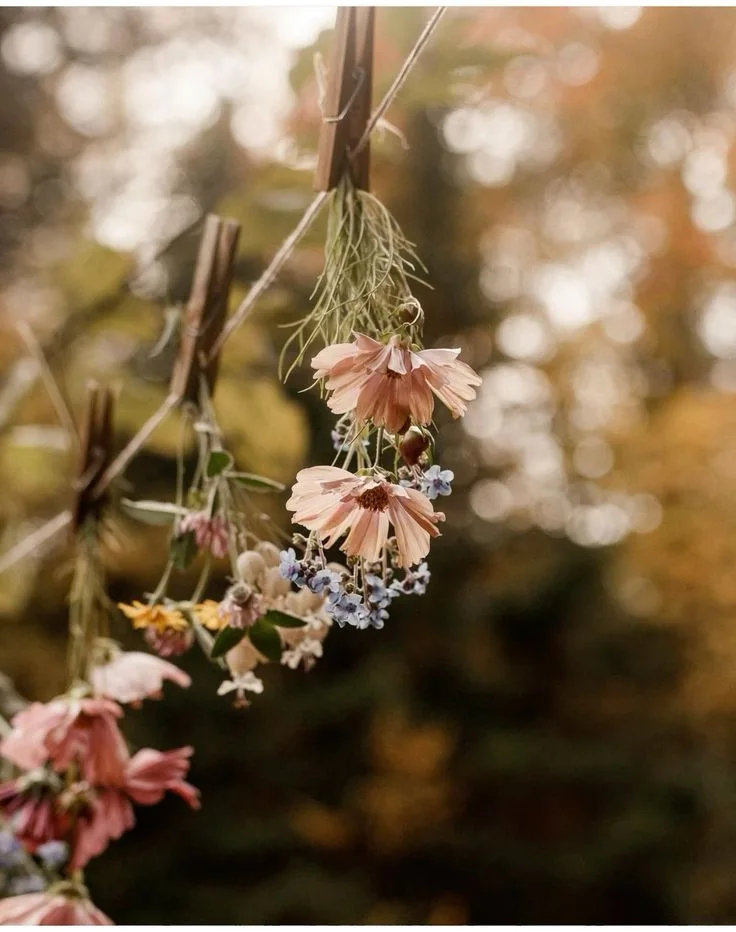 A light floral garland hanging among branches in warm woodland light.