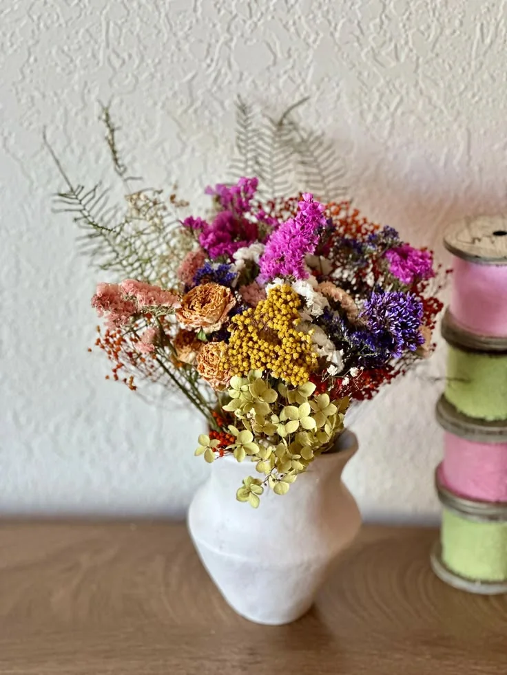 A white ceramic vase with colourful dried botanicals and airy foliage.
