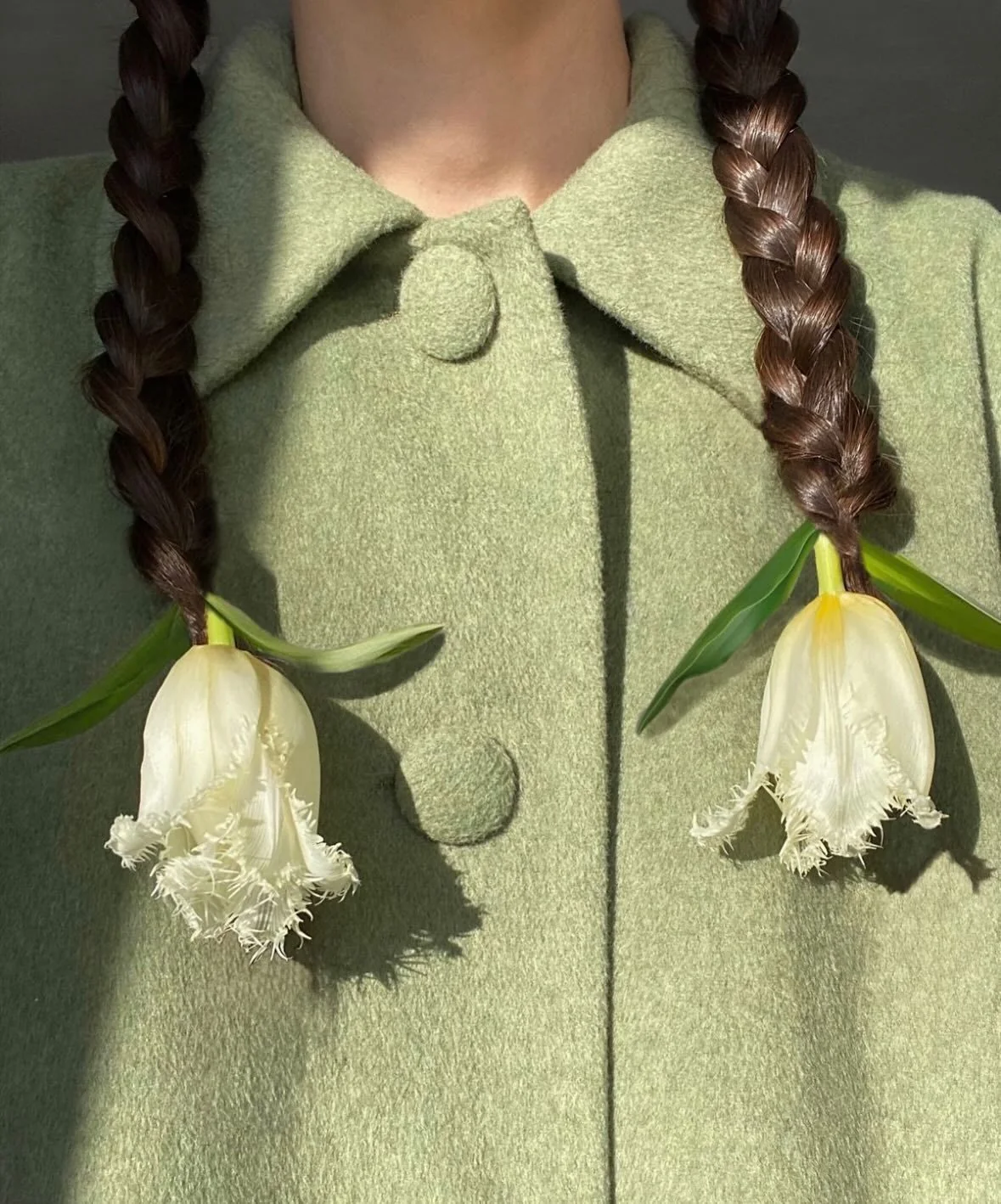 White tulips and green leaves arranged as hanging details beside braided hair.